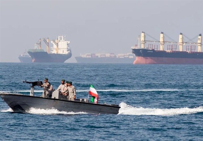 Một tàu quân sự của Iran tại eo biển Hormuz, phía sau là một số tàu thương mại - Ảnh: MEHR