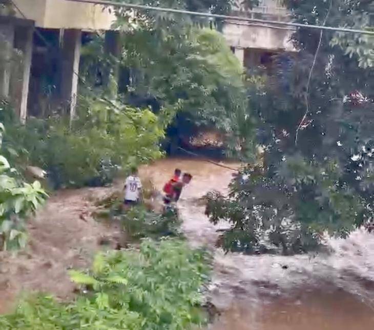 Anh Kiên đưa lần lượt hai em nhỏ vượt qua dòng nước đang dâng để vào bờ an toàn. Ảnh: VY MẰN.