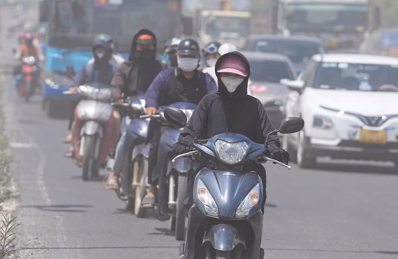 Hàng dài người lái xe máy lưu thông dưới chân cầu Thăng Long phải đeo khẩu trang và đội mũ trùm kín mặt để bảo vệ hệ hô hấp khỏi bụi mịn.
